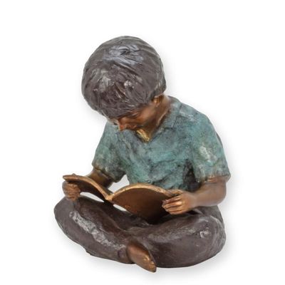 A BRONZE SCULPTURE OF A YOUNG BOY READING A BOOK
